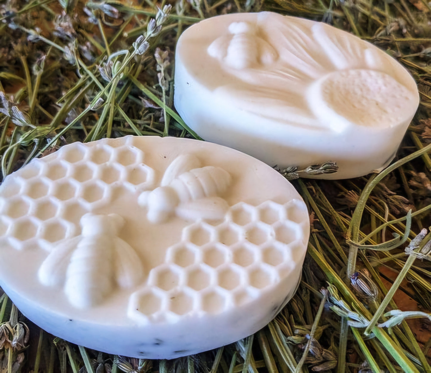 Oval-shaped artisan soaps in a silicone mold. Some of the soaps contain visible dried herbs, while others have intricate designs of bees, honeycomb, and flowers. The mix of textured and smooth soap surfaces showcases natural ingredients and handcrafted quality, perfect for promoting a rustic, eco-friendly product line.