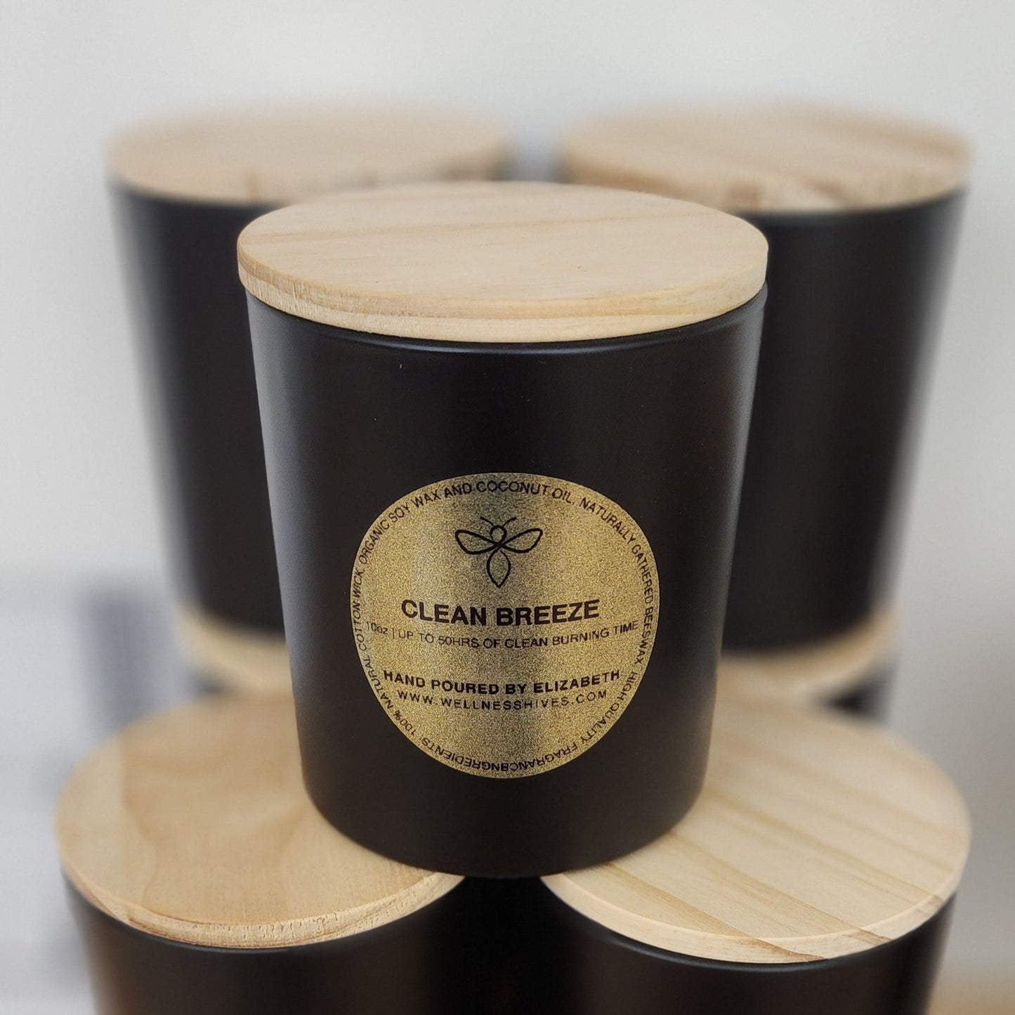 A black jar candle labeled 'Clean Breeze,' hand-poured by Elizabeth from wellnesshives.com, featuring a wooden lid and made with organic soy and coconut wax, offering up to 50 hours of clean burning time Clean Breeze 10oz Organic Candle 50hr