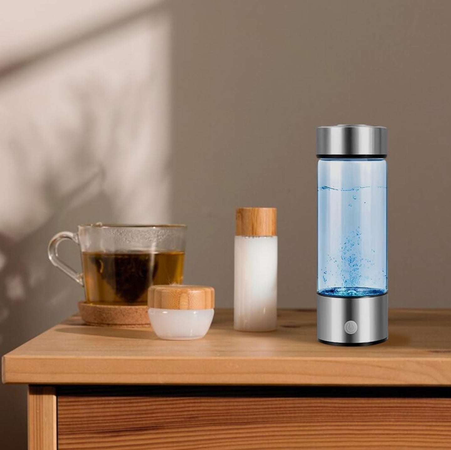 Hydrogen water bottle alongside a glass cup of tea, a small container, and a bottle with a bamboo lid, all placed on a wooden table, creating a calm and minimalistic setting.