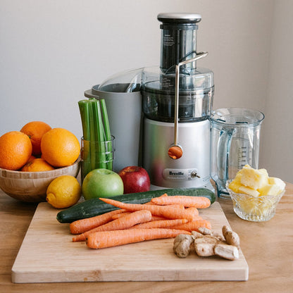 A variety of fresh fruits and vegetables, including carrots, ginger, oranges, celery, cucumber, and pineapple, displayed on a kitchen counter next to a juicer, ready for juicing as part of a health and wellness routine