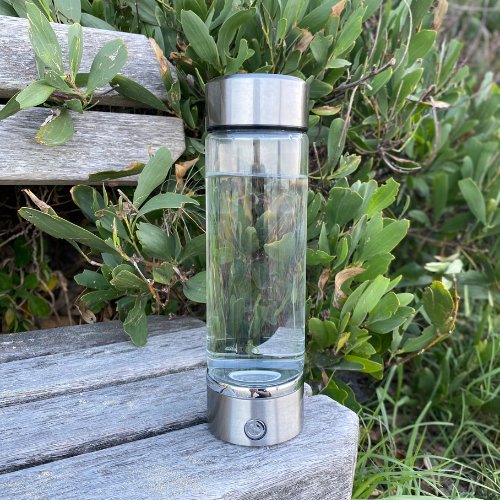 Hydrogen water bottle placed on a wooden bench outdoors, with lush green plants in the background. 