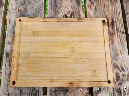 A 9.5 x 13 bamboo cutting board displayed flat on a rustic wooden table. The cutting board has rounded corners and small holes in each corner, showcasing its functional yet stylish design. The natural bamboo grain and smooth surface make it a durable and eco-friendly addition to any kitchen for chopping or serving.