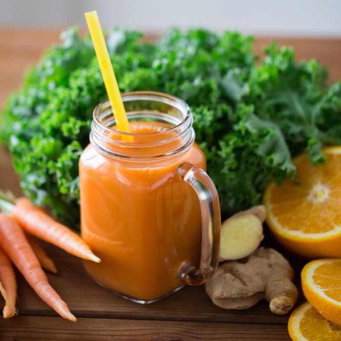 A mason jar filled with bright orange juice and a straw, surrounded by fresh ingredients including carrots, ginger, kale, and sliced oranges, highlighting a nutritious juice recipe from a health and wellness ebook.