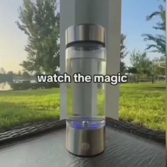 Promotional image for a hydrogen water bottle showcasing the product outdoors on a wooden surface with a green park backdrop. The video thumbnail features the water bottle with a caption overlay reading 'watch the magic' at the base, highlighting the transformative experience of using the product.